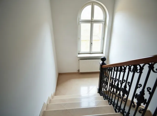 Sauberes, helles Treppenhaus eines Münchner Altbaus mit gewischten Steinstufen und gepflegtem Holzhandlauf